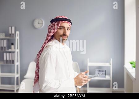 L'uomo arabo serio e penoso guarda in un ufficio bianco. Foto Stock
