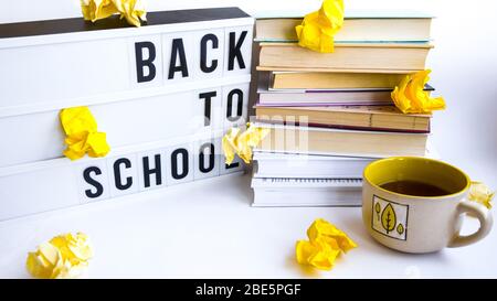 Scatola luminosa con testo DI RITORNO A SCUOLA e libri su sfondo bianco con carta gialla sbriciolata Foto Stock