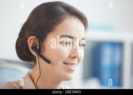 Ritratto della testa e delle spalle di una giovane donna sorridente che indossa le cuffie e parla con il cliente mentre lavora nel call center o nel servizio di assistenza, spazio per la copia Foto Stock