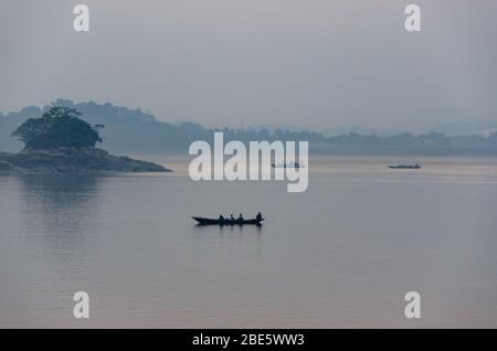 Silhouette di un gruppo di uomini che giravano una piccola barca sul fiume Might Brahmaputra durante il tramonto a Guwahati, Assam, India Foto Stock