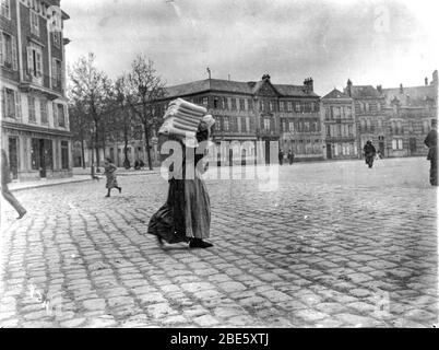 Una vecchia signora porta un cesto di biancheria sulla schiena attraverso le strade acciottolate di Dieppe nel 1890 Foto Stock