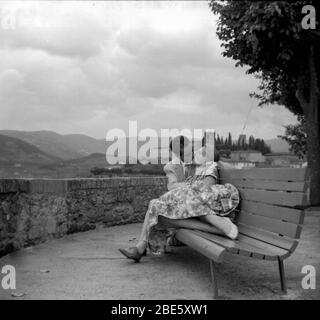 Una giovane coppia ben vestita abbraccio e bacio su una panchina negli anni Cinquanta a Montecatini, in Toscana Foto Stock
