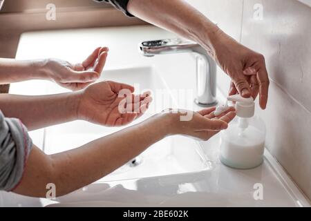 Madre che insegnava a sua figlia come lavare correttamente le loro mani con sapone per prevenire l'infezione da coronavirus Foto Stock