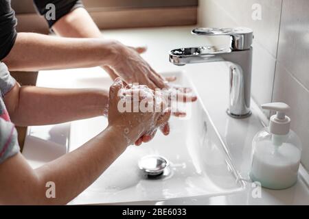 Madre che insegnava a sua figlia come lavare correttamente le loro mani con sapone per prevenire l'infezione da coronavirus Foto Stock