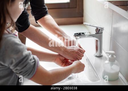 Madre che insegnava a sua figlia come lavare correttamente le loro mani con sapone per prevenire l'infezione da coronavirus Foto Stock