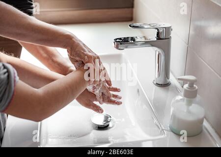 Madre che insegnava a sua figlia come lavare correttamente le loro mani con sapone per prevenire l'infezione da coronavirus Foto Stock