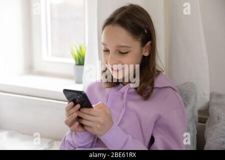 Sorridente ragazza teen utilizzando le app per telefoni cellulari a casa Foto Stock