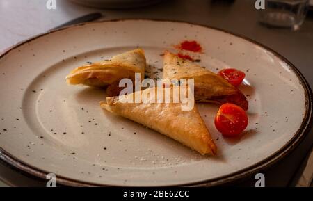 samosa fatti in casa sul piatto con piccoli pomodori, cucina casalinga. bloccato all'interno. Foto Stock