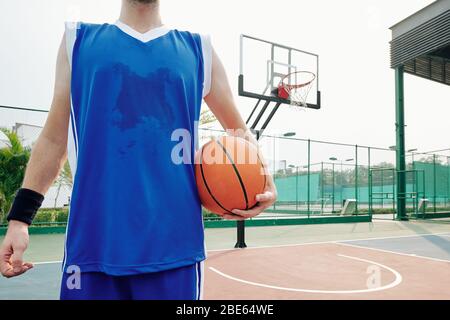 Immagine ritagliata del giocatore di basket sudato che si trova sul campo da gioco all'aperto con palla Foto Stock