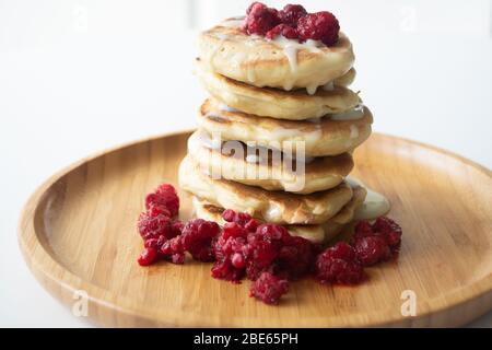 Frittelle soffici con latte condensato e lamponi su un piatto di legno con tovagliolo da cucina e forchetta Foto Stock