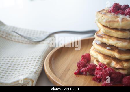 Frittelle soffici con latte condensato e lamponi su un piatto di legno con tovagliolo da cucina e forchetta Foto Stock