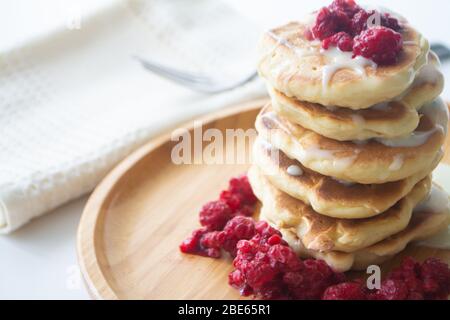 Frittelle soffici con latte condensato e lamponi su un piatto di legno con tovagliolo da cucina e forchetta Foto Stock