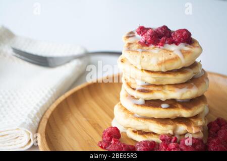 Frittelle soffici con latte condensato e lamponi su un piatto di legno con tovagliolo da cucina e forchetta Foto Stock