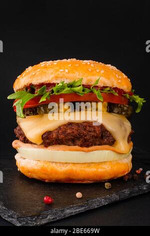 Un grande hamburger classico hamburger cheeseburger alto su sfondo nero Foto Stock