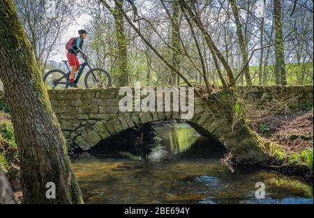 bella donna di mezza età in mountain bike a un piccolo fiume in una calda giornata di primavera soleggiata Foto Stock
