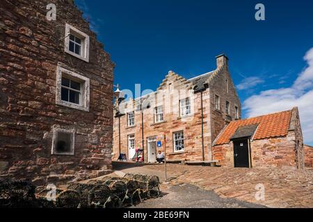 Un uomo locale siede su una panchina fuori da un edificio in pietra intorno al porto di pescatori, Crail, Regno di Fife, Scozia, Europa Foto Stock