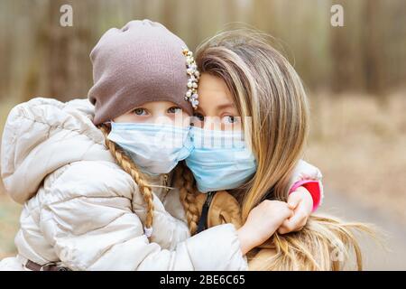 Mamma e figlia in maschere mediche per la strada durante la pandemia covid-19. Concetto sul tema delle passeggiate in quarantena Foto Stock