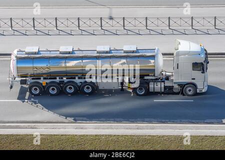 Grande e pesante cisterna con serbatoio in metallo lucido zoppo guida su autostrada città, vista aerea laterale Foto Stock