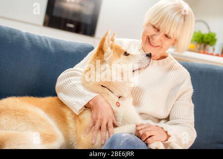 Pensionamento. Donna anziana seduta a casa abbracciando Husky siberiano sorridendo felice primo piano Foto Stock