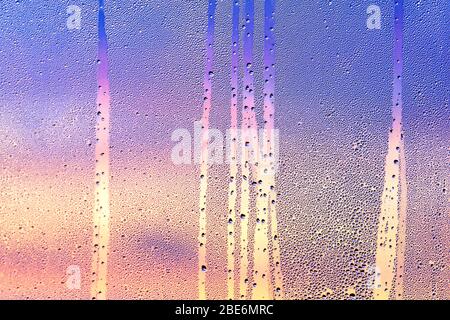 Consistenza delle gocce d'acqua sul vetro con tramonto magenta sullo sfondo. Condensa sulla finestra trasparente. Pioggia. Foto Stock