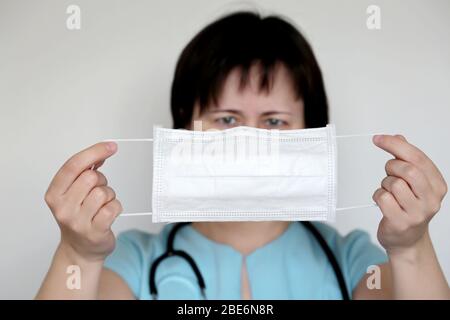 Protezione da coronavirus, la donna indossa una maschera medica. Medico con maschera di influenza bianca nelle sue mani, concetto di quarantena covid-19 Foto Stock