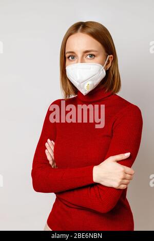 Studio ritratto di donna in un dolcevita rosso con maschera facciale - respiratore N95 con filtro laterale, isolato su sfondo grigio. Influenza, allergia alla polvere, pr Foto Stock