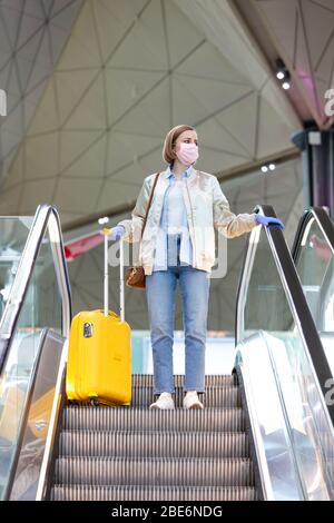 Donna con bagagli gialli si trova sulla scala mobile presso il terminal dell'aeroporto quasi vuoto a causa di restrizioni di viaggio per l'epidemia di coronavirus/Covid-19. Foto Stock