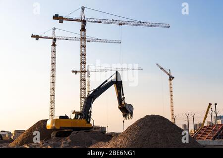 Gru a torre e silhouette degli escavatori in cantiere, sfondo cielo al tramonto. Futuro complesso residenziale di alto livello Foto Stock