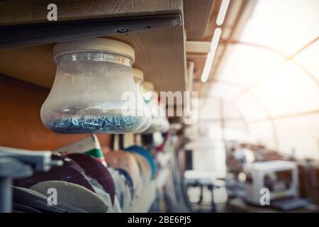 Interni di officina in legno con molti attrezzi e attrezzature differenti. Vasi in plastica con molte viti diverse chiodi sospesi su scaffale per Foto Stock