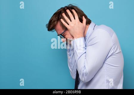Frustrato giovane manager maschile chiudendo le orecchie con le mani che sono irritate e stressate. Scatto studio Foto Stock