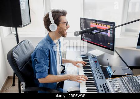 L'uomo suona chitarra e canto e produce colonna sonora elettronica o traccia in progetto a casa. Arrangiatore di musica maschile che compone canzone su midi piano e audio Foto Stock