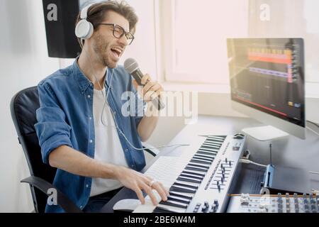 L'uomo canta nel microfono e lavora sul mixer audio in studio di registrazione o DJ in studio di trasmissione. Produttore di musica sta componendo una canzone su Foto Stock