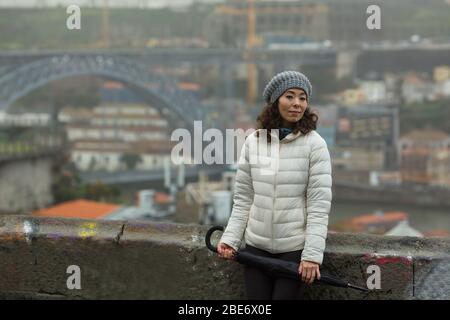 Donna asiatica in nebbia sullo sfondo del ponte Dom Luis i a Porto, Portogallo. Foto Stock