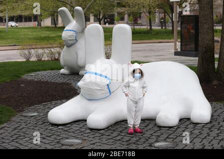 St. Louis, Stati Uniti. 12 aprile 2020. Little Emilie Aylott (4) tira il suo vestito coniglietto come lei ha una foto scattata, in City Garden a St. Louis Domenica, 12 aprile 2020. I conigli del Giardino della Città si proteggono anche con maschere chirurgiche, durante la Pandemia di Coronavirus. Foto di Bill Greenblatt/UPI Credit: UPI/Alamy Live News Foto Stock