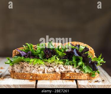 Sandwich di tonno e lattuga su pane di segale su superficie in legno con sfondo di lino Foto Stock