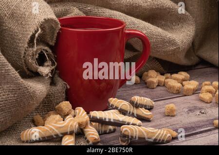 Tazza in ceramica rossa con tè, bastoncini di biscotto con cioccolato e glassa bianca su sfondo di legno. Primo piano Foto Stock