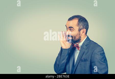 Uomo d'affari nel profilo che sussurra un segreto di pettegolezzo o un sicuro informazioni personali guardando la macchina fotografica che vi dice circa un affare grande. Gara mista bea Foto Stock