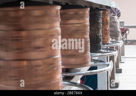 Ruota di preghiera in un tempio buddista a Varanasi con una vecchia signora che prega con le perle di preghiera Foto Stock