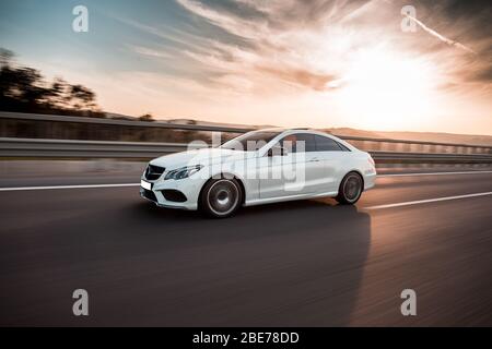 Auto di lusso bianca al tramonto sotto il cielo blu Foto Stock