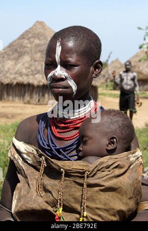 Ritratto di una giovane madre Karo Tribe che tiene il suo bambino addormentato vicino al suo torace Foto Stock