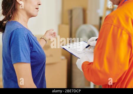Cliente maturo che parla con la mover che sta compilando i dettagli nel documento di servizio di consegna Foto Stock