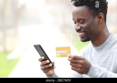 Black man shopper pagare online con carta di credito su smartphone in un parco Foto Stock