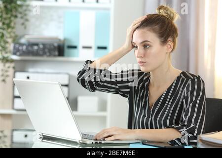 Una donna sorpresa che commette errori online lavorando su un notebook seduto su una scrivania a casa Foto Stock