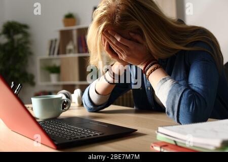 Primo piano di studenti tristi che ricevono cattive notizie sul notebook seduto su una scrivania a casa di notte Foto Stock