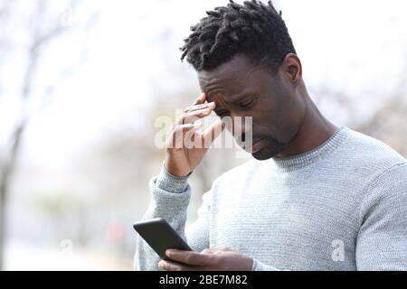 Uomo nero preoccupato che legge le cattive notizie sullo smartphone in piedi al parcheggio