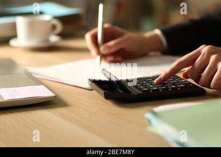Primo piano di donna imprenditore mani contabilità utilizzando calcolatrice di notte su una scrivania a casa Foto Stock