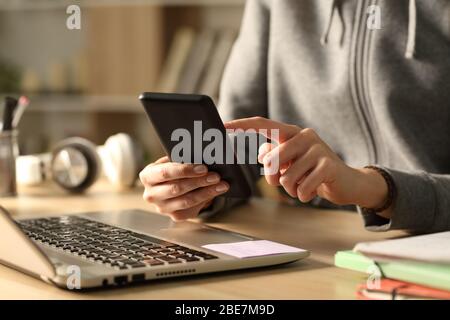 Primo piano delle mani della ragazza studentesca che controllano lo smartphone di notte seduto a casa Foto Stock