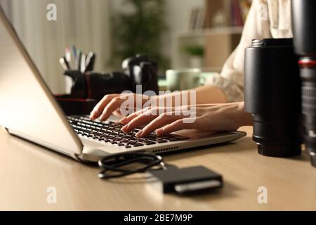 Primo piano di una donna fotografo che trasfida i file delle schede di memoria al laptop di notte su una scrivania a casa Foto Stock