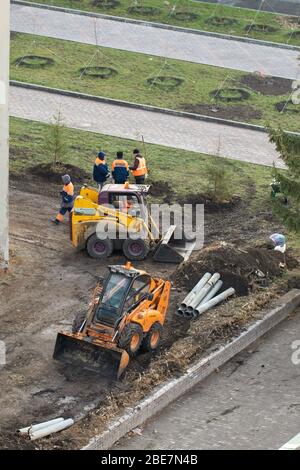 Bulldozer costruzione e costruzione di nuova strada asfaltata vicino a edifici civili. Concetti di miglioramento del territorio degli edifici. Alloggi e servizi di pubblica utilità co Foto Stock