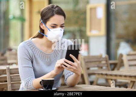 Donna seria con maschera protettiva evitando contagio controllare notizie su smartphone in un bar Foto Stock